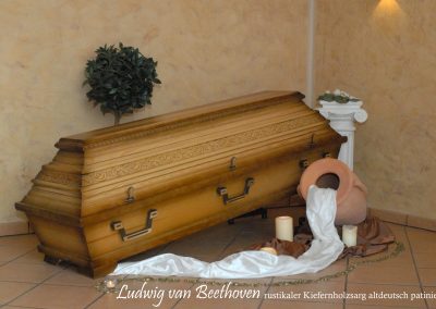Ein Holzsarg ruht ruhig auf einem gefliesten Boden, umgeben von weichem Stoff. In der N&auml;he werfen Kerzen einen warmen Schein auf eine Urne und eine kleine Pflanze &ndash; der perfekte Rahmen f&uuml;r eine herzliche Bestattung.