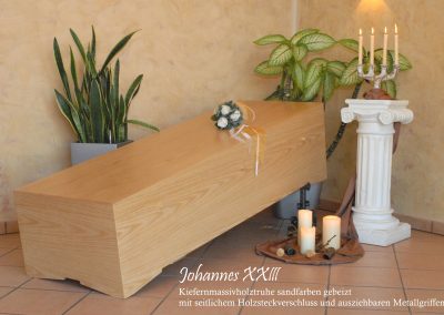 Ein Holzsarg mit einem kleinen Blumenstrau&szlig; steht sanft zwischen Pflanzen und Kerzen, flankiert von einer dekorativen S&auml;ule, die mit einer Menora geschm&uuml;ckt ist, und schafft so eine heitere Bestattungsatmosph&auml;re.
