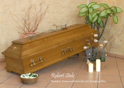 Ein Holzsarg mit Messinggriffen ruht feierlich auf dem gefliesten Boden, begleitet von flackernden Kerzen, anmutig arrangierten Pflanzen und einem kleinen Korb &ndash; und schafft so eine heitere Umgebung f&uuml;r eine respektvolle Bestattung.
