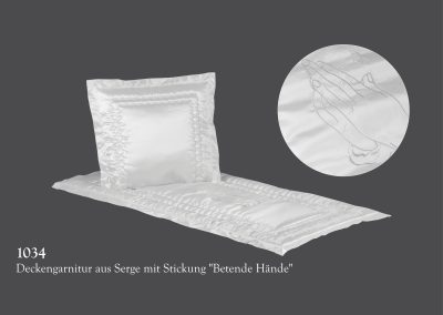 Kissen und Bezug aus wei&szlig;em Satin mit Stickerei betender H&auml;nde, die oft bei Bestattungszeremonien verwendet und vor einem dunklen Hintergrund dargestellt werden.