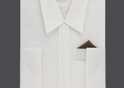 Elfenbeinfarbenes Herrenhemd mit braunem Einstecktuch, kunstvoll auf grauem Hintergrund angeordnet, verleiht einen eleganten und feierlichen Touch, der an die Kleidung einer Bestattung erinnert.